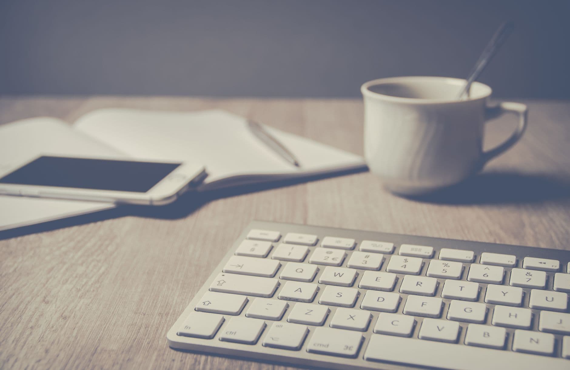 Un bureau rangé et lumineux : un carnet ouvert, une tasse et un clavier