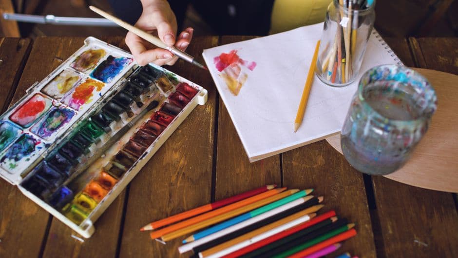 Palette d'aquarelle, pinceaux et carnet sur une table près d'une verrière