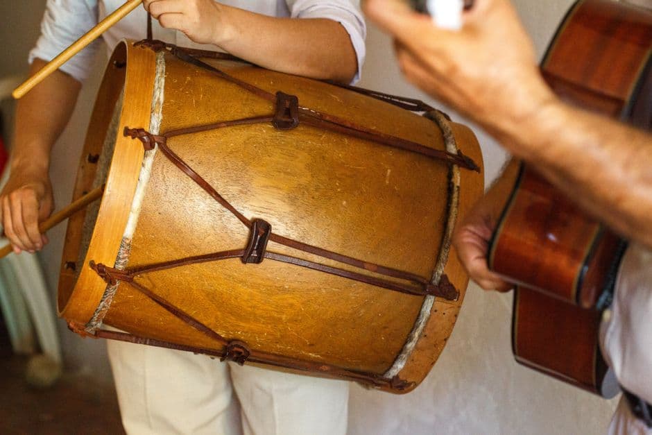 Tambour en bois tenu à deux mains, une guitare à côté