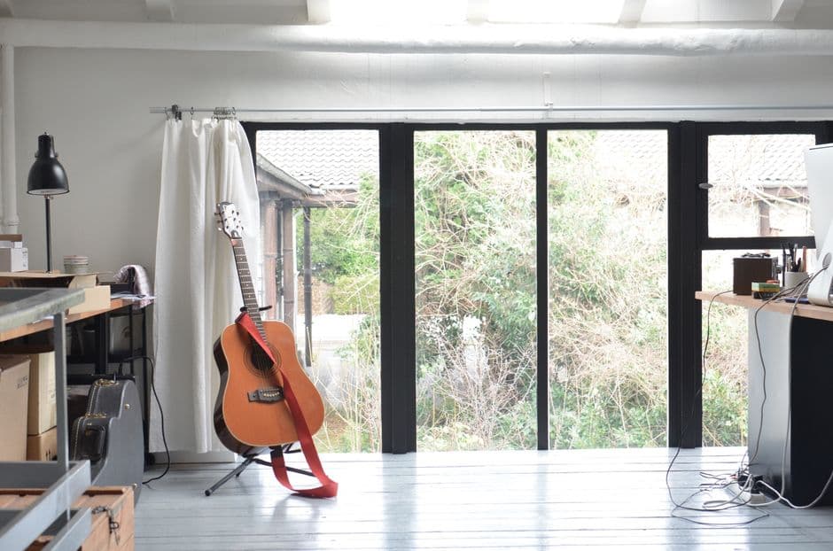 Guitare acoustique posée sur un pied devant la baie vitrée d'une salle de répétition