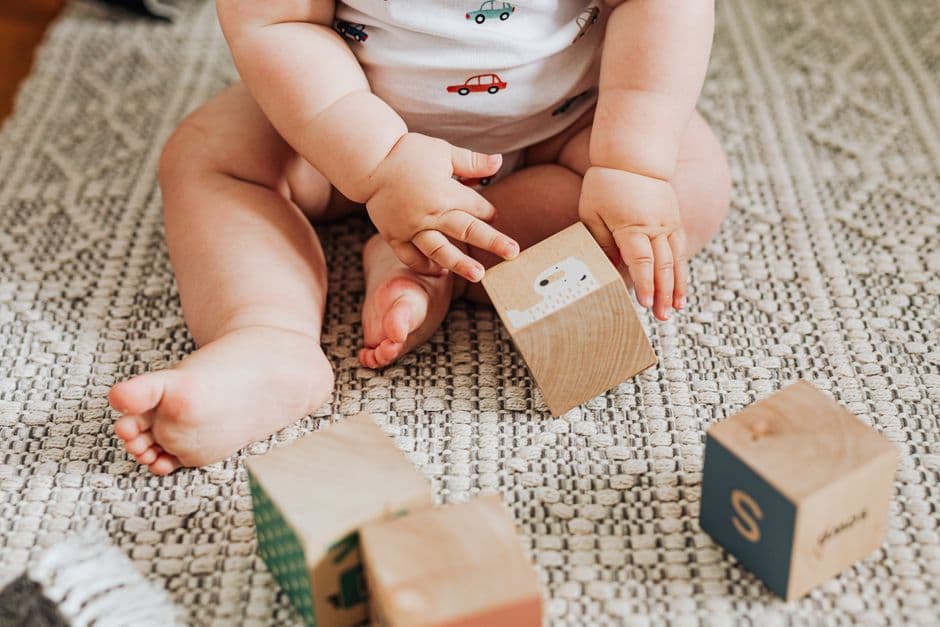 Cubes en bois et mains d'un tout-petit assis sur un tapis clair