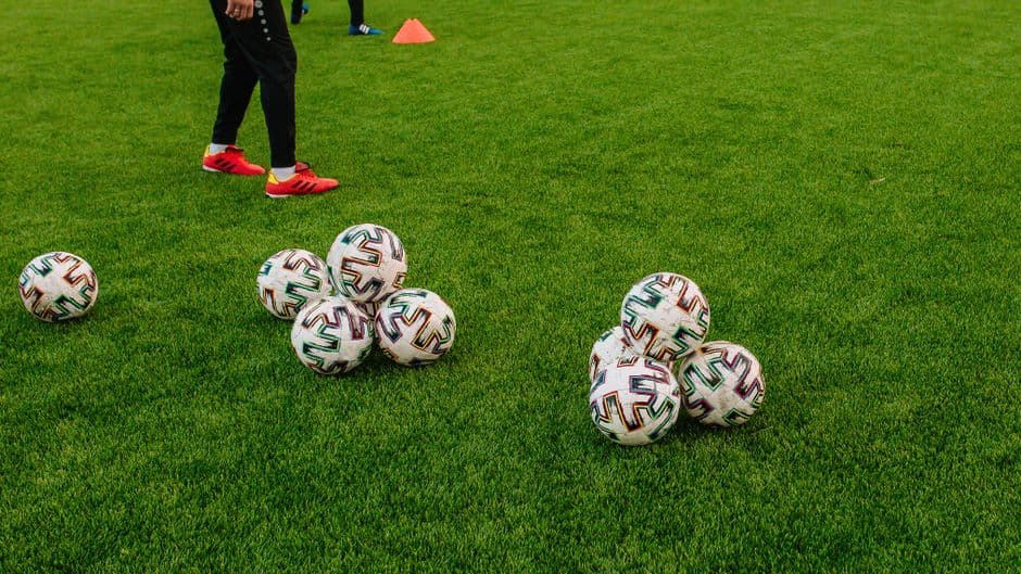 Ballons de football et plot orange posés sur une pelouse synthétique